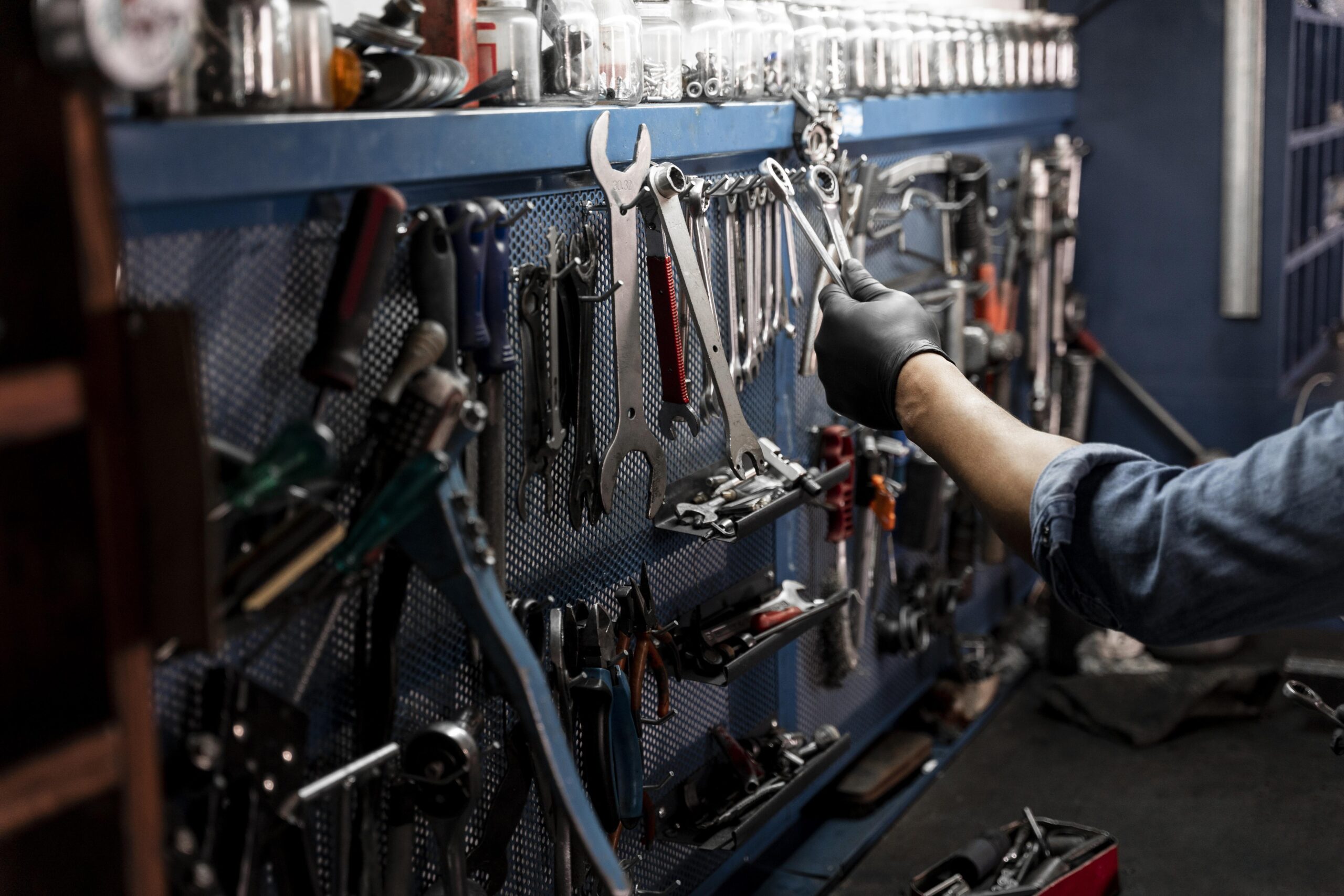 Arm reaches for a wrench from a wall of various tools.